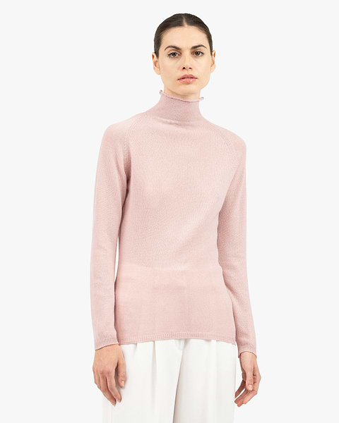 Woman in blush pink turtleneck sweater with white trousers
